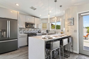 A modern kitchen with a central island, stainless steel appliances, and pendant lighting. - Pool + Hot Tub + Fire Pit | Outdoor Kitchen | Near Indian Canyons | Hercules (Palm Springs)