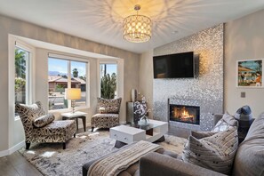 A living room with a fireplace, patterned chairs, a sofa, and a television. - Pool + Hot Tub + Fire Pit | Outdoor Kitchen | Near Indian Canyons | Hercules (Palm Springs)