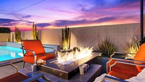 A poolside area with a fire feature, orange chairs, and a brick wall.