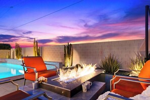 A poolside area with a fire feature, orange chairs, and a brick wall. - Pool + Hot Tub + Fire Pit | Outdoor Kitchen | Near Indian Canyons | Hercules (Palm Springs)