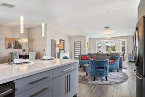 A modern kitchen with a large island, dining area with chairs, and a living room with sofas. - Pool + Hot Tub + Fire Pit | Outdoor Kitchen | Near Indian Canyons | Hercules (Palm Springs)