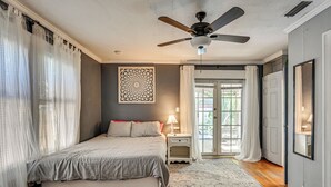 Een slaapkamer met een bed, een plafondventilator, een nachtkastje, een lamp, een kamerbreed tapijt met dessin, en een deur die leidt naar een balkon.