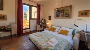 A hotel room with a bed, a desk, a chair, a window with curtains, and a painting on the wall. - Casa dello Scrittore (Florence)