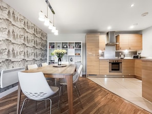 Eine moderne Küche mit Holzausbau, einem eingebauten Backofen und einem Essbereich mit Holztisch und weißen Stühlen.
