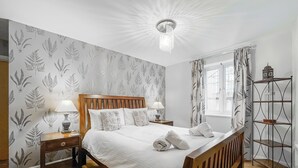 Quarto bem arrumado com cama de madeira, duas mesas de cabeceira com luminárias, uma janela com cortinas e uma estante de metal.