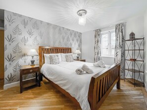 Ein ordentlich eingerichtetes Schlafzimmer mit einem Holzbett, zwei Nachttischen inklusive Lampen, einem Fenster mit Vorhängen und einer Metallregaleinheit.