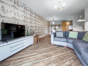Ein modernes Wohnzimmer mit Flachbildfernseher, grauem Sofa, Holzboden und strukturierter Tapete.
