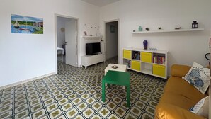 Ein Wohnzimmer mit Fernseher, einem grünen Sessel, einem gelben Bücherregal und einem gemusterten Boden.