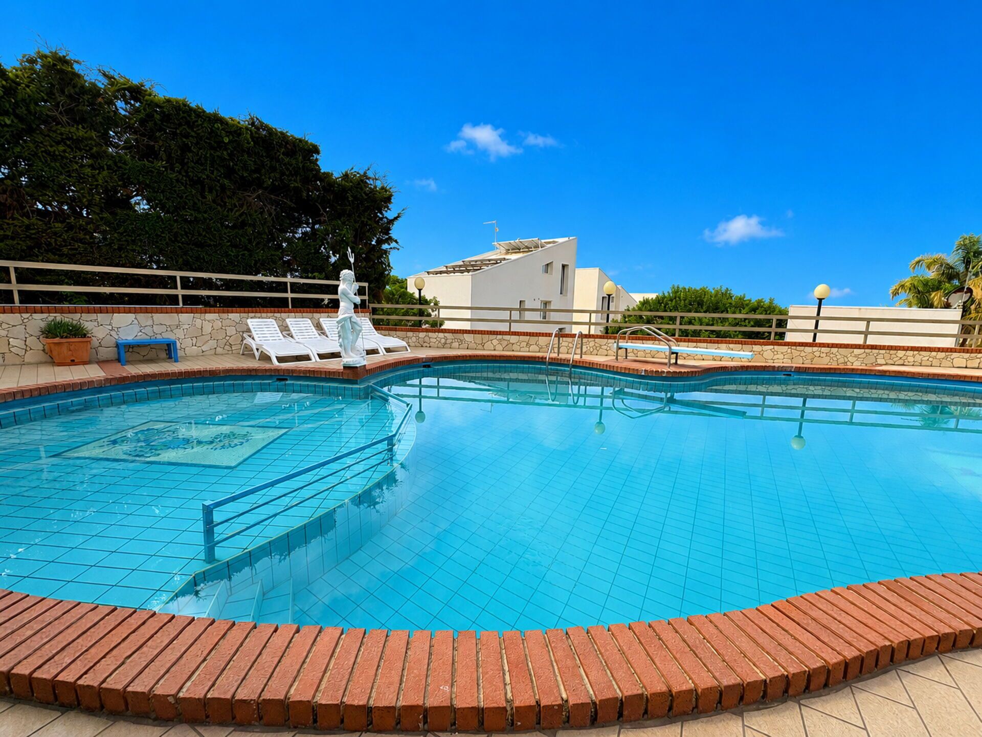 Una piscina con borde de azulejos, una estatua y sillas de descanso.