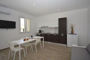 A modern kitchen with white cabinets, a dining table with chairs, a flat-screen TV, and a grey sofa. - Villa Benvenuti al Sud (Roccazzo)