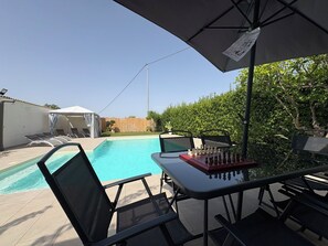 A poolside area with a table and chairs, a chessboard, and a covered seating area.