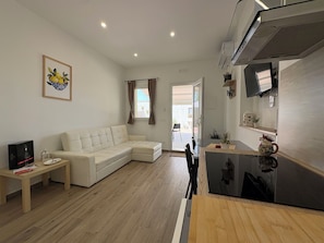 A living room with a sofa, a small table, and a kitchen area with a counter and appliances.