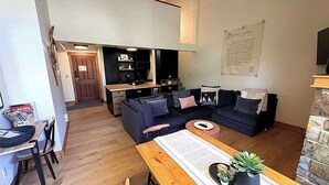Un salon moderne avec un canapé bleu foncé, une table à manger en bois et un coin cuisine à l’arrière-plan.