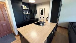 Une cuisine de taille réduite, dotée d’un plan de travail en bois, de meubles de rangement noirs et d’un four à micro-ondes.