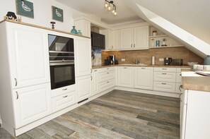 A kitchen with white cabinets, a built-in oven, a coffee maker, and a wooden countertop. - House Clemens - Apartment Julius: Balcony (Mönchgut)
