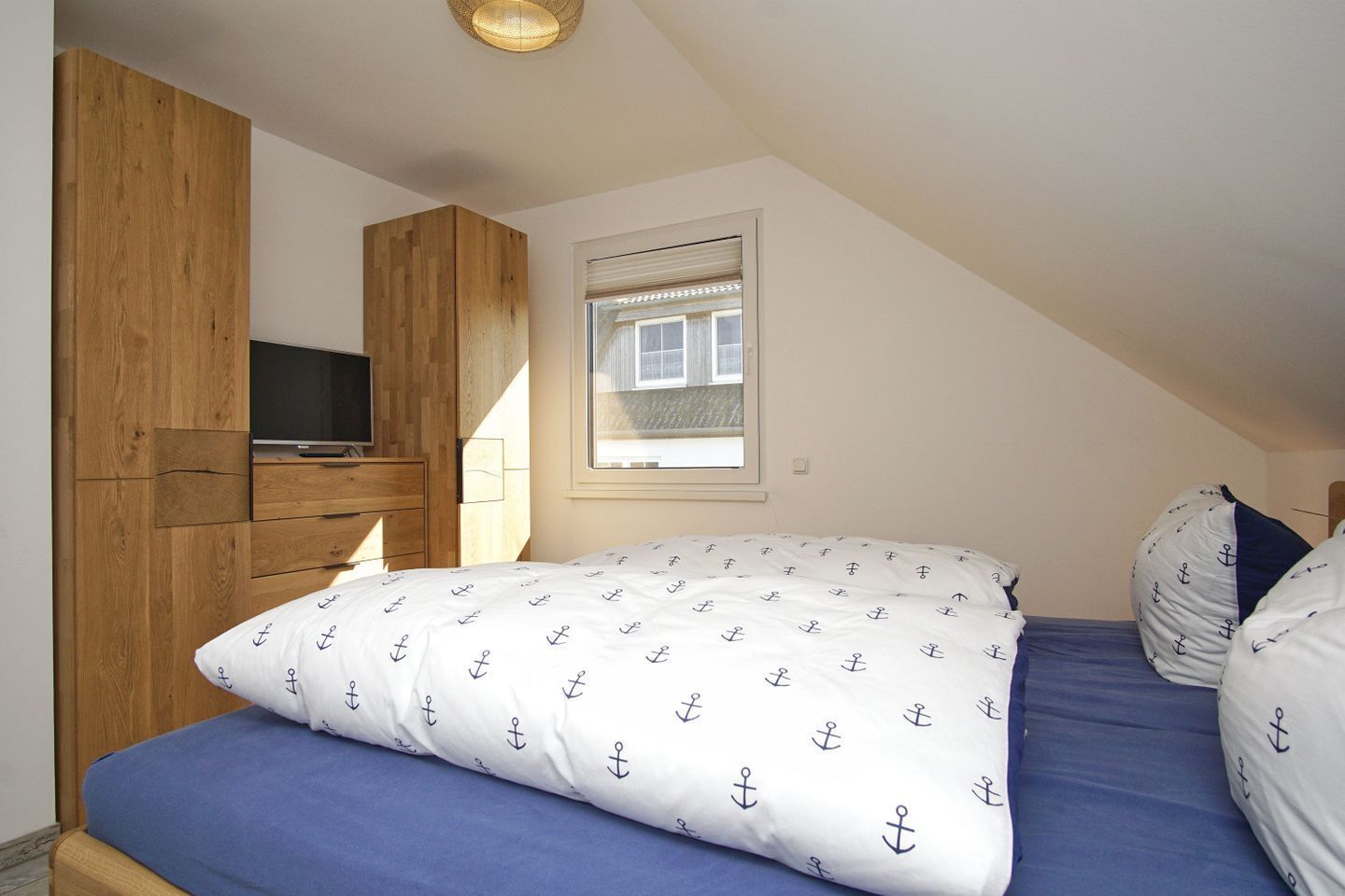 Ein Schlafzimmer mit einem Bett, einem Fernseher, einem Holzschrank und einem Fenster mit Jalousien.