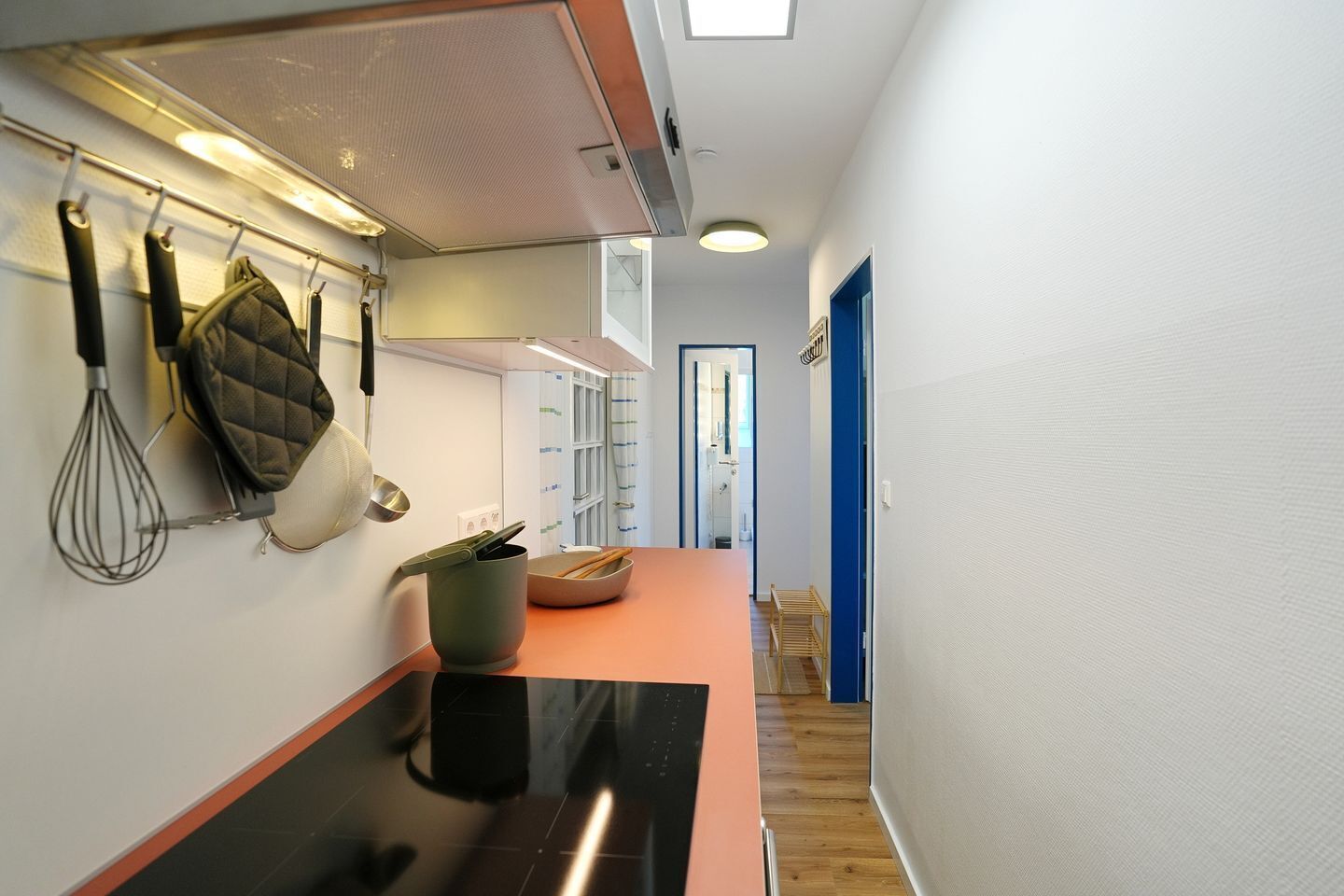 A modern kitchen with a black countertop, hanging kitchen utensils, and a view into the adjacent room.