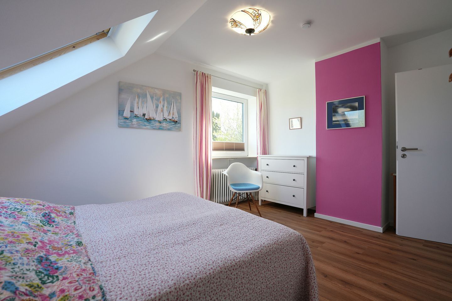 A bedroom with a bed, a chair, a dresser, a window with curtains, and a painting on the wall.