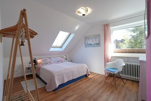 Ein Schlafzimmer mit Oberlicht, einem Bett mit floralem Überwurf, einem Schreibtisch, einem Stuhl und einer Heizung.