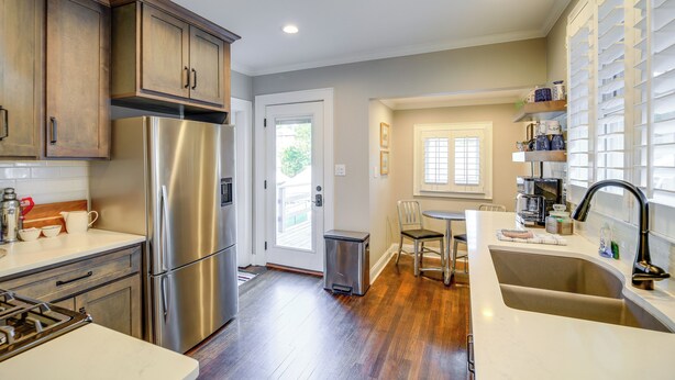 Una cocina con refrigerador de acero inoxidable, armarios de madera, un lavamanos y una zona de comedor con una silla y una mesa.