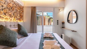 A hotel room with a stone wall, a bed with pillows, a bedside table with a vase, and a view through a glass door. - Two Bedroom Villa with Private Pool (Rhodes)