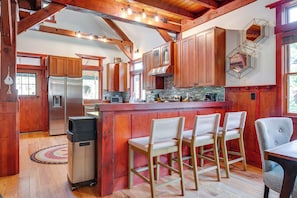 A kitchen with wooden cabinets, a stainless steel refrigerator, and a bar area with bar stools. - Hot Tub, Game Room! Stunning Home By Short Sands (York)