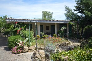 Ein Gebäude mit einem Ziegeldach, grünen Fensterläden und einem Garten mit verschiedenen Pflanzen und Blumen.
