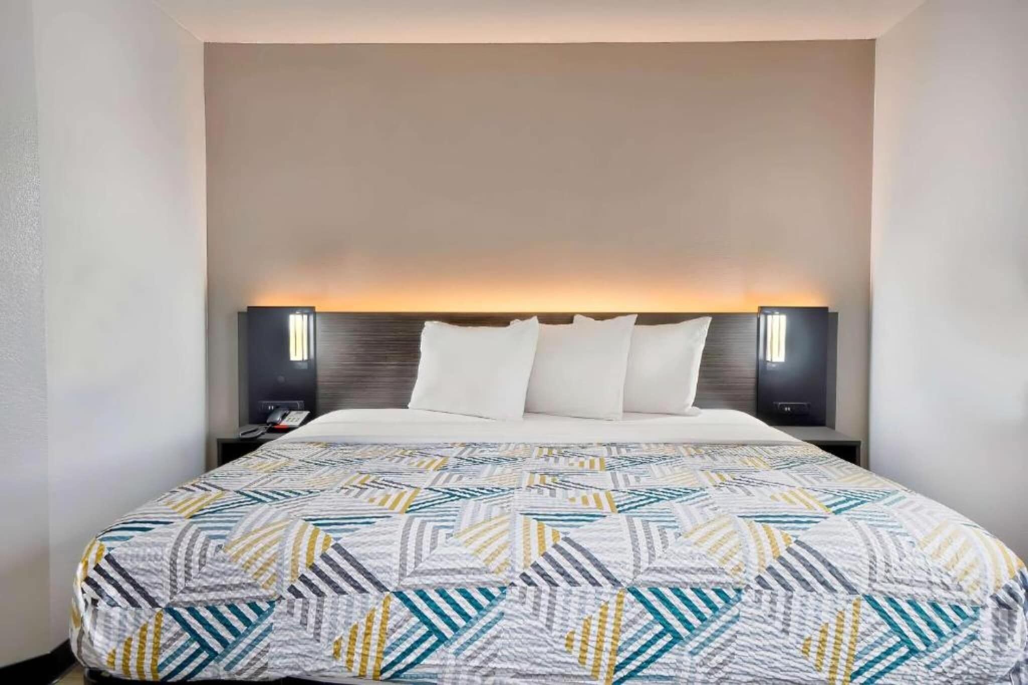 A hotel room with a bed, a nightstand, and two wall-mounted lamps.