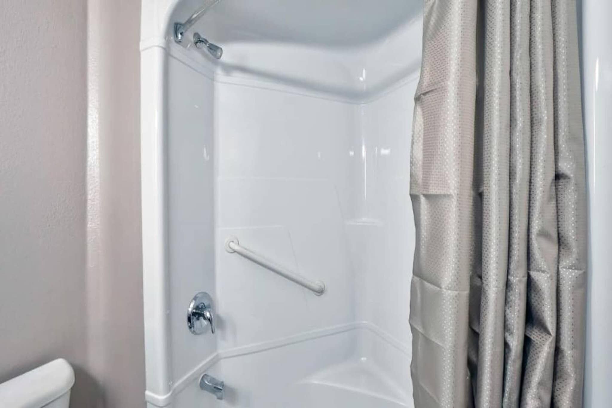 A corner shower with a clear glass door, a white towel rack, and a beige shower curtain.