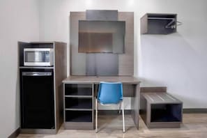 Een kleine kamer met een kitchenette, een bureau, een stoel en een televisie die aan de muur is bevestigd.