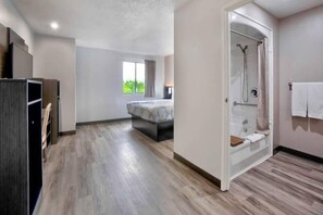 Ett modernt hotellrum med en stor säng, en rymlig dusch och utsikt över grönområden utanför.