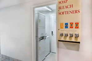 Passadís amb una porta que condueix a la sala de la bugaderia, un dispensador fixat a la paret per sabó, lleixiu i suavitzants, i un senyal que indica que el dispensador s'ha de bloquejar quan estigui buit.