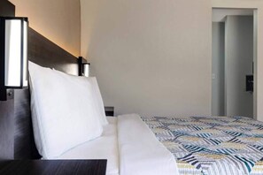 A hotel room with a bed, a nightstand, a bedside table, and a door leading to another room. - 1 King Bed  Non-Smoking (Shepherdsville)