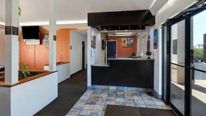 Un área de recepción con mostrador, televisión y vista a través de puertas de vidrio.