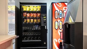 A vending machine with snacks and beverages, a Coca-Cola dispenser, and a sign for 'BLEACH SOFTENERS'. - 1 King Bed | Mobility Accessible Tub, Nsmk (Shepherdsville)