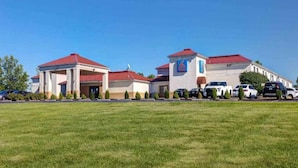 A hotel with a red roof, a number '6' sign, and a parking lot with several cars. - 1 King Bed | Mobility Accessible Tub, Nsmk (Shepherdsville)