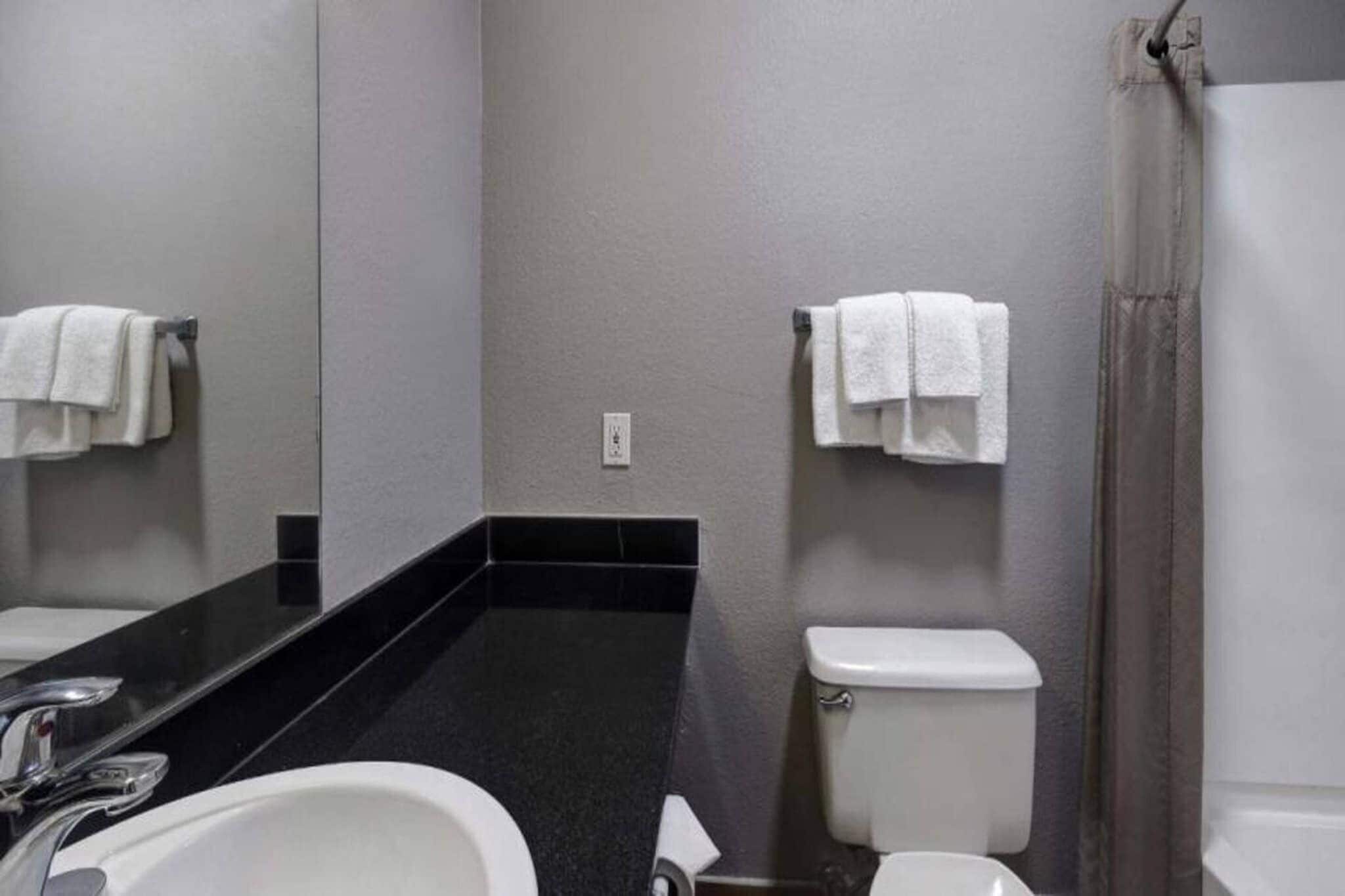A bathroom with a black countertop, white sink, and toilet. There are towels hanging on the wall.