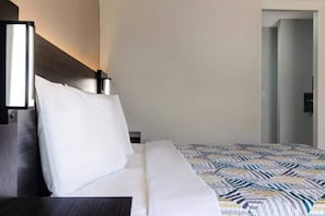 A hotel room with a bed, a nightstand, a bedside table, and a door leading to another room. - 1 King Bed | Smoking (Shepherdsville)