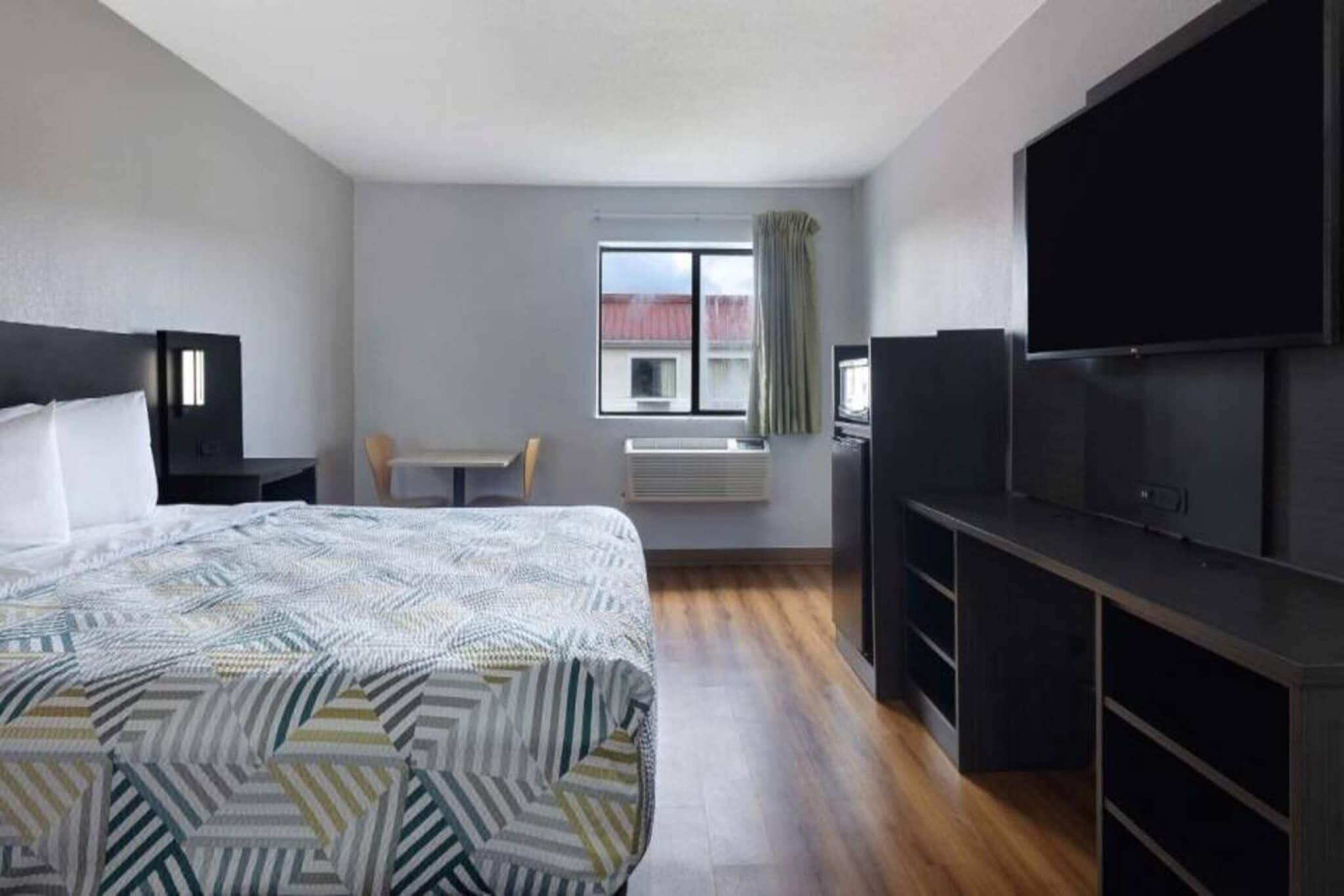 Una habitación de hotel con cama, escritorio, televisor y ventana con cortinas.