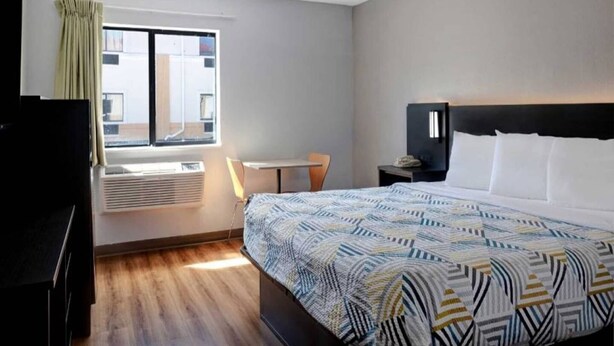 A hotel room with a bed, a desk, a chair, a TV, and a window with curtains. - 1 King Bed | Smoking (Shepherdsville)