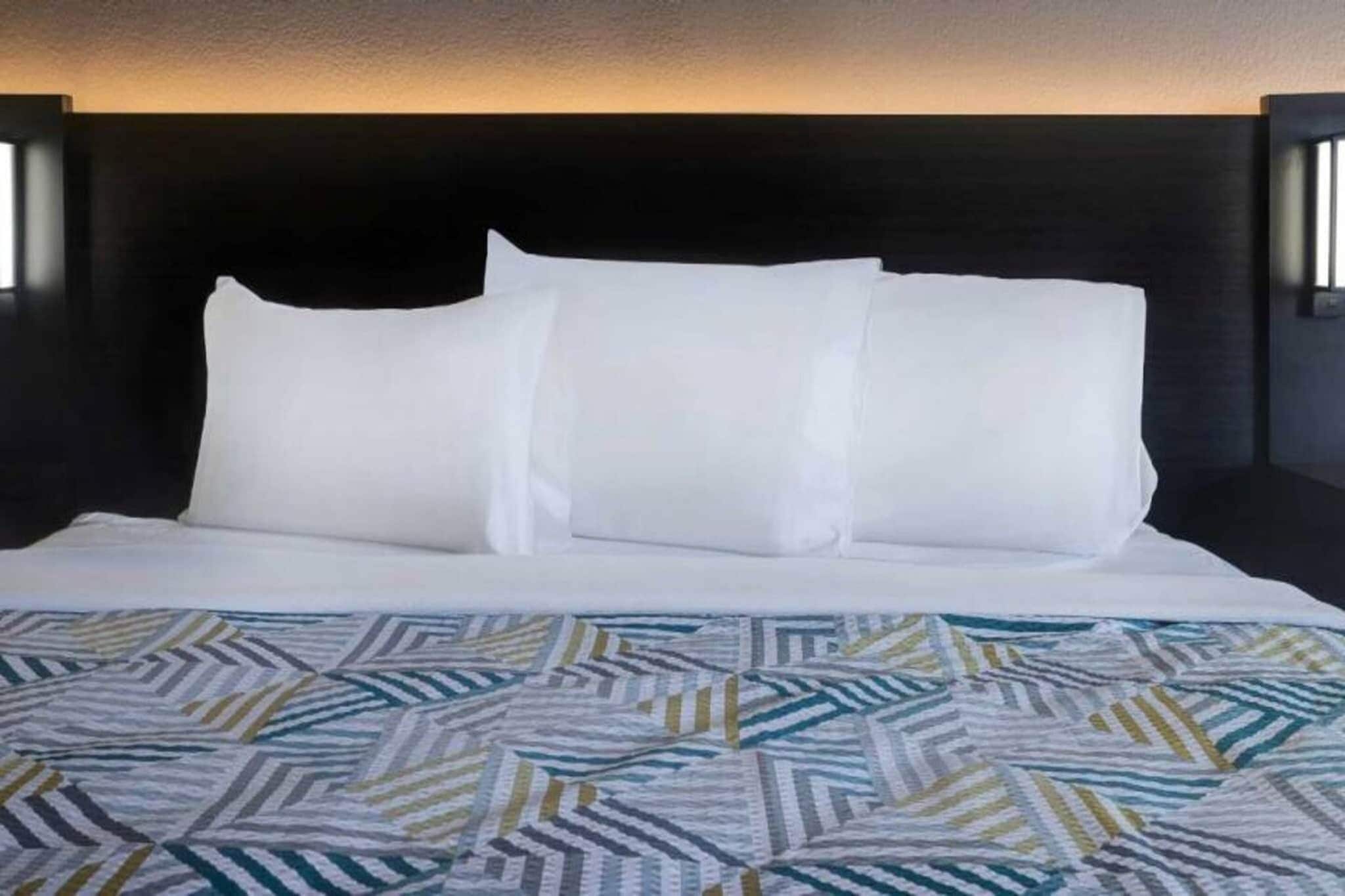 Un lit avec une literie blanche et un couvre-lit à motifs, une tête de lit sombre et des appliques murales.