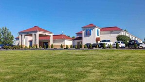 A hotel with a red roof, a number '6' sign, and a parking lot with several cars. - 1 King Bed | Smoking (Shepherdsville)