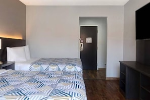 A hotel room with a bed, a desk, a TV, and a door leading to another room.
