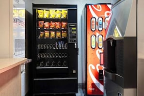 Een automaat met snacks en dranken, een Coca-Cola dispenser en een bordje met 'BLEACH SOFTENERS'.