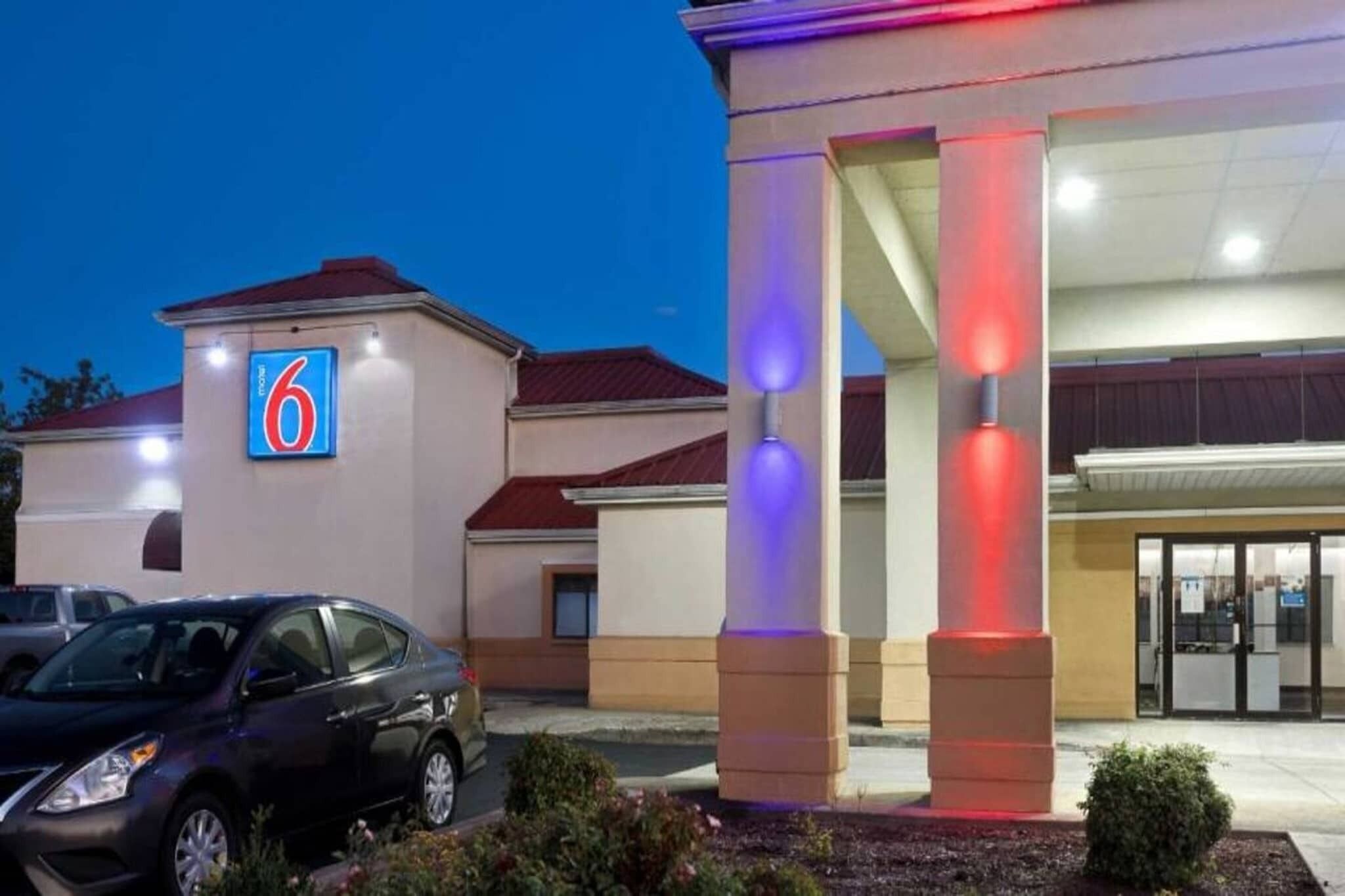 L’entrée d’un hôtel, avec un grand panneau indiquant le chiffre « 6 », un espace de stationnement couvert et un bâtiment doté d’un toit rouge.