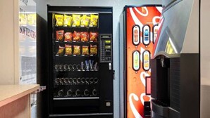 A vending machine with snacks and beverages, a Coca-Cola dispenser, and a sign for 'BLEACH SOFTENERS'. - 2 Queen Beds | Smoking (Shepherdsville)