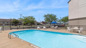 A rectangular pool with a metal ladder, surrounded by a fence. There are lounge chairs and a table with umbrellas.