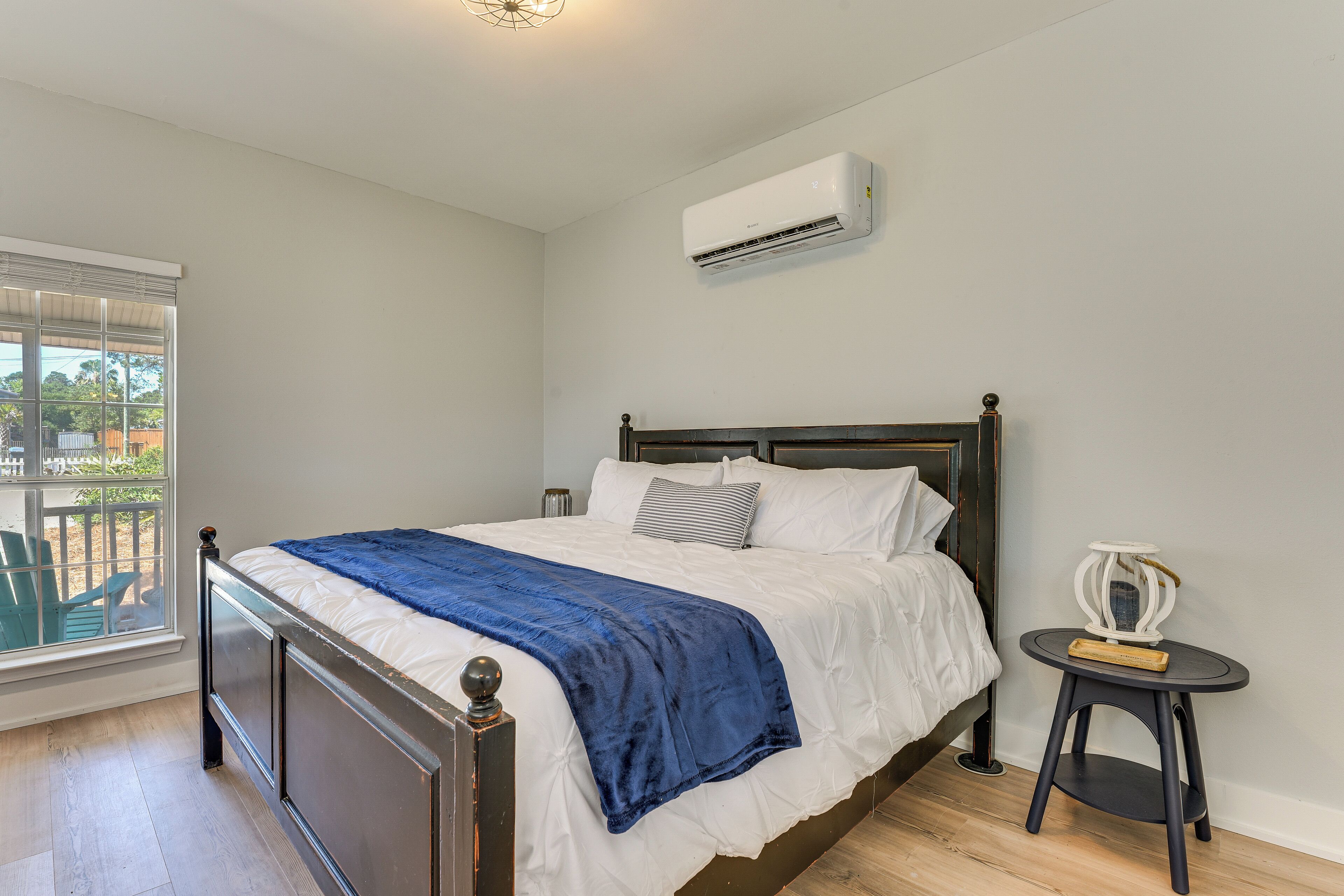 A bedroom with a bed, an air conditioner, a window, and a small table.