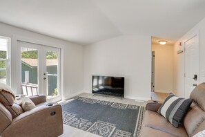 Un salon équipé d’un téléviseur, de deux canapés, d’un tapis à motifs et d’une porte-fenêtre coulissante donnant sur un espace extérieur.
