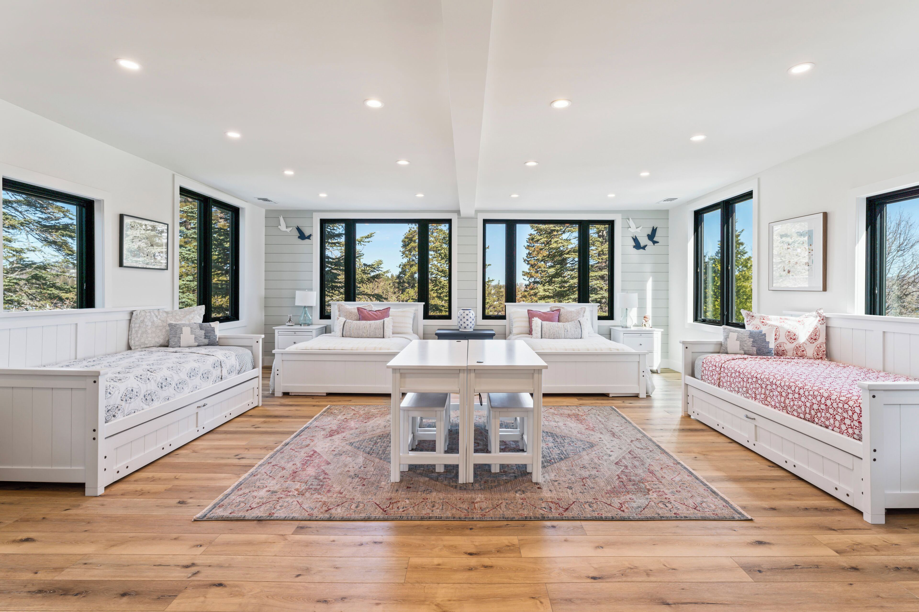 Una habitación amplia con una cama grande, dos zonas de estar, una mesa de comedor y ventanas grandes con vistas a árboles.